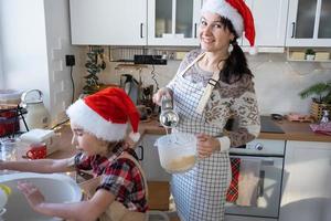 mamma e figlia nel il bianca cucina impastare il Impasto nel il ciotola per Pan di zenzero e biscotti con un' miscelatore per Natale e nuovo anno. foto