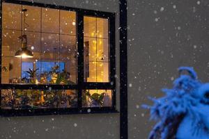 accogliente festivo finestra di il Casa al di fuori con il caldo leggero di Fata luci ghirlande dentro - celebrare Natale e nuovo anno nel un' caldo casa. Natale albero, bokeh, neve su pino alberi e nevicata foto