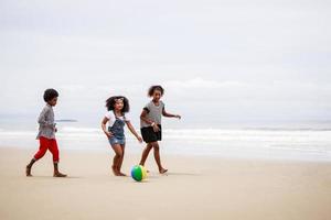 gruppo di africano americano bambini giocare palla e avere divertimento su un' tropicale spiaggia foto
