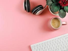 piatto posare di computer tastiera del computer, rosa caffè tazza, cuffie e africano violette nel pianta pentola su rosa sfondo con copia spazio. foto