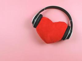 piatto posare di rosso cuore cuscino coperto con cuffie su rosa sfondo. amore canzoni o Podcast concetto. foto