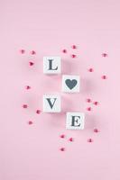amore Messaggio scritto nel bianca di legno blocchi su sfondo. rosa caramella cuori. piatto posizione, superiore Visualizza foto