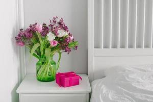 rosa scatola presente e vaso con primavera fiori su comodino vicino letto. scandinavo interno. foto