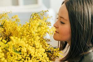 giovane ragazza in piedi con un' mazzo di giallo mimosa e odorare fiori. concetto di vacanza primavera foto