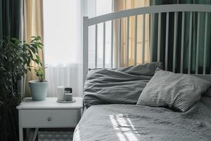 Camera da letto con leggero interno. moderno candela, casa pianta su capezzale tavolo vicino letto. casa stile di vita foto