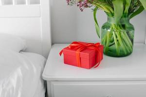 mazzo di tulipani e rosso regalo scatola su il comodino nel il Camera da letto. womans giorno, madri giorno foto