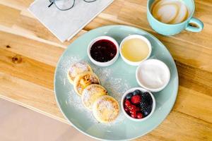 salutare estate prima colazione. Villetta formaggio Pancakes, cappuccino caffè su di legno tavolo. superiore Visualizza foto