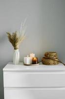 casa interno arredamento nel beige neutro colori. bianca costumista con secco fiori nel vaso, malacca borse e candela. ancora vita, hygge concetto foto