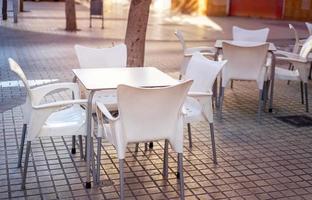 bianca plastica tavolo circondato di sedie su il terrazza di un' piccolo bar foto