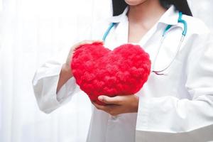 un' bellissimo asiatico donna medico Tenere un' grande rosso cuore. nel il trattamento camera. ospedale paziente cura concetti foto