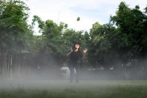 asiatico corto capelli donna è gioioso salto nel il nebbia ambiente su erba campo giardino. foto