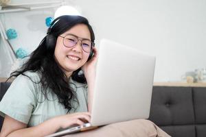 bicchieri bellissimo asiatico donna è Lavorando su sua il computer portatile nel il Camera da letto con un' pastello verde - Marrone colore tema. foto