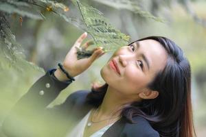 attraente, fiducia giovane asiatico donna nel attività commerciale nero completo da uomo è pubblicazione, sorridente nel davanti di le foglie e albero con un' rilassante umore nel il giardino a pomeriggio volta. foto