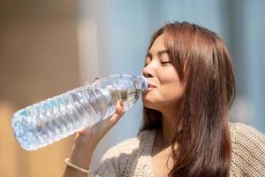 asiatico donna bevande grande bottiglia acqua nel all'aperto verde bokeh albero sfondo. foto