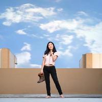 asiatico donna sta e sorrisi solo con detiene stivali su tetto nel pastello blu - Marrone ombra. foto