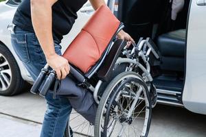 donna asiatica che piega e solleva la sedia a rotelle nella sua auto. concetto di accessibilità. foto