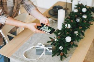 giovane donna nel plaid camicia prende foto regalo scatola su festivo tavolo con il abete composizione, Natale tempo