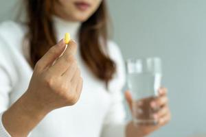 vicino su di mani donna Tenere un' dietetico supplemento o medicazione o vitamina e un' bicchiere di acqua pronto per prendere. assistenza sanitaria, medicina, cura di sé, malattia e farmacia concetto. foto