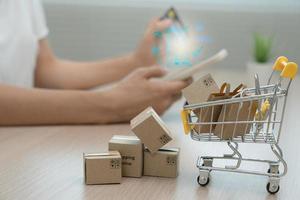 in linea scatole della spesa o pacchi siamo posto su il tavolo e shopping carrelli. sfocato sfondo, donna uso credito carta per rendere in linea acquisti su il computer portatile. in linea servizio. nuovo normale shopping consegna. foto