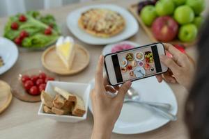 la mano di un recensore che utilizza un telefono cellulare per scattare foto del cibo al tavolo di un ristorante. Scatta una foto per scrivere una recensione del ristorante da condividere su Internet.