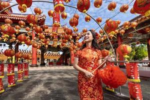 asiatico donna nel rosso cheongsam qipao vestito Tenere lanterna mentre visitare il Cinese buddista tempio durante lunare nuovo anno per tradizionale cultura concetto foto