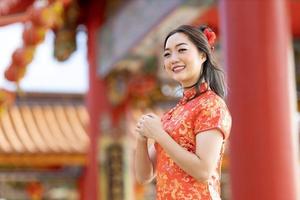 asiatico donna nel rosso cheongsam qipao vestito è fabbricazione un' desiderio per ancestrale Dio dentro Cinese buddista tempio durante lunare nuovo anno per per migliore desiderio benedizione e bene fortuna foto