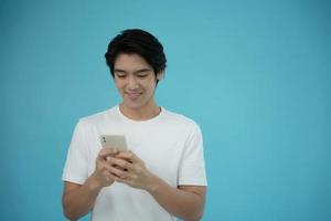 bello asiatico uomo sorridente contento con il suo Telefono su leggero blu sfondo. foto
