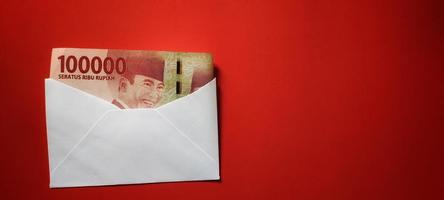indonesiano rupia banconote di valore idr 100.000 nel un' bianca Busta isolato su rosso sfondo foto