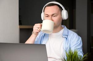 avvicinamento ritratto di giovane asiatico con cuffie su uomo potabile caffè e ascoltando per podcast, musica ot avere video chiama.lavoro a partire dal casa. in linea formazione scolastica foto