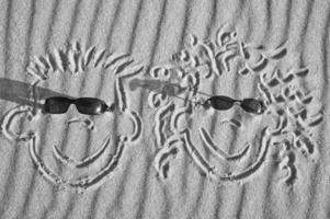 viso disegnato nel il sabbia su il spiaggia, con occhiali da sole. sabbia con onda modello foto