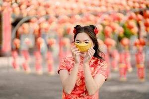 contento Cinese nuovo anno. un' giovane signora indossare tradizionale cheongsam qipao vestito Tenere antico oro i soldi nel Cinese buddista tempio. celebrare Cinese lunare nuovo anno, festivo stagione vacanza. foto