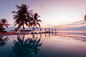 lusso nuoto piscina su il spiaggia, tranquillo scena di esotico tropicale paesaggio con copia spazio, estate sfondo per vacanza vacanze. bellissimo bordo piscina e tramonto cielo. lussuoso tropicale spiaggia foto