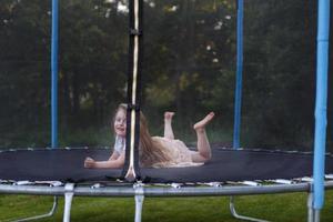 poco bambino ragazza salto su il trampolino nel il indietro cortile foto