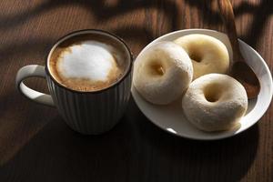 caldo latte macchiato e ciambelle su di legno tavolo dietro a finestra foto