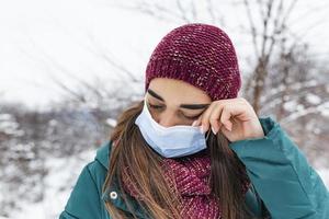 evitare toccante il tuo occhi. donna indossare viso maschera sfregamento sua occhio all'aperto. giovane donna toccante sua occhio con sporco mano. non fare toccare il tuo viso, fermare diffusione coronavirus foto