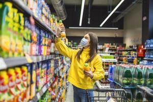 donna indossare viso maschera acquisto drogheria nel supermercato durante covid-19 pandemia. femmina con un' shopping carrello acquisto alcuni cibo elementi nel supermercato. foto