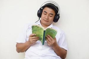 asiatico uomo legge libro e indossa cuffie ascolta per morbido musica per rendere concentrazione nel lettura. concetto, gratuito volta, passatempo, passatempo, rilassare con musica. foto