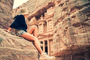 caucasico turista viaggiatore sedersi su punto di vista nel petra antico città guardare a il tesoreria o al-khazneh, famoso viaggio destinazione di Giordania. unesco mondo eredità luogo foto