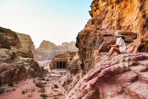 donna viaggiatore turista seduta su punto di vista nel petra antico città, antico storico luogo famoso viaggio destinazione di Giordania e uno di Sette meraviglie. unesco mondo eredità luogo foto