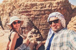 caucasico coppia turista sedersi su punto di vista nel petra antico città al di sopra di tesoreria o al-khazneh prendere smartphone foto insieme. Giordania, uno di Sette meraviglie. unesco mondo eredità luogo.