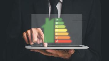 persona mano utilizzando digitale tavoletta con Casa icona energia efficienza scala Immagine su buio sfondo, concetto di ecologico e bio energico Casa. energia classe. foto