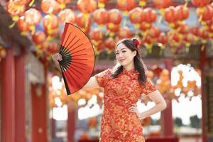 asiatico donna nel rosso cheongsam qipao vestito Tenere carta fan mentre visitare il Cinese buddista tempio durante lunare nuovo anno per tradizionale cultura concetto foto