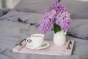 prima colazione nel letto. vassoio con caffè e un' mazzo di lillà su il letto nel il Camera da letto foto