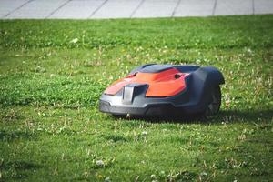 prato falciatore rosso robot su verde tagliare erba su soleggiato giorno nel un' parco foto