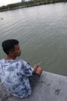 gorontalo-indonesia, dicembre 2022 - un' adolescenziale ragazzo è pesca su il Riva del fiume nel il pomeriggio foto