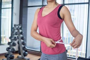 dieta donne siamo misurazione vita con nastro nel il palestra. esercizio concetto per bene Salute e bellissimo forma foto