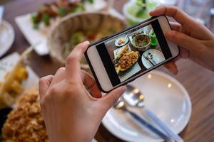 donna utilizzando mobile Telefono per prendere immagini di cibo su il tavolo. prese su mobile e mettere su sociale reti. foto