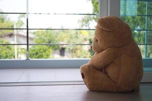 maggiore depressivo disturbo mdd concetto. dolore di bambini. orsacchiotto orso seduta guardare a il Casa finestra solo. sembra piace qualcuno chi è triste, deluso, depresso foto