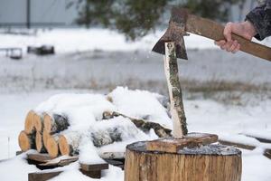 un' uomo è chopping legna da ardere con un ascia nel inverno all'aperto nel il neve. alternativa il riscaldamento, legna raccolta, energia crisi foto