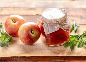 pieno piccolo bicchiere vaso con Mela marmellata e Due mele e greem menta su di legno sfondo. foto